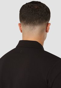 Zwarte poloshirt, gladde stof, korte mouwen, platte kraag, minimale logo-detail op de achterkant. Schoon, minimalistisch ontwerp geschikt voor casual dragen.