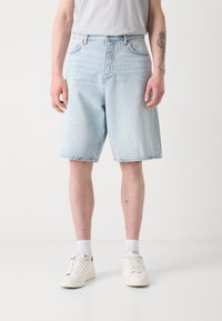 Shorts en denim bleu clair avec une coupe ample, design à cinq poches et ourlet droit. Associés à des baskets blanches et des chaussettes mi-mollet.