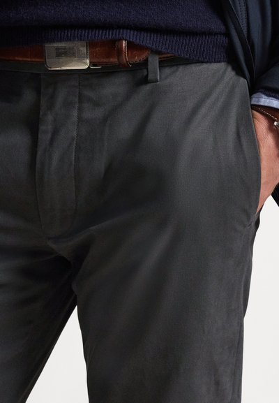 Fekete nadrág sima textúrával, oldalzsebekkel, finom elülső hajtással, valamint barna bőrből készült övvel, fém csattal.