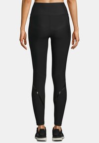 Czarne legginsy sportowe z wysokim stanem, gładką teksturą i błyszczącymi panelami po bokach; noszone z czarnymi butami sportowymi.