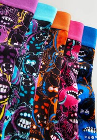 Calcetines coloridos con tejido negro y diseños vibrantes de monstruos en azul, rosa, naranja y púrpura, acentuados con puños de color contrastante.