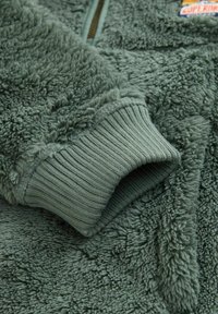 Fleecejacke in gedämpftem Grün mit strukturiertem, weichem, fellähnlichem Stoff. Verfügt über gerippte Bündchen und einen Frontreißverschluss. Mit Logo-Tag akzentuiert.