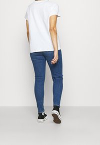 Bílý krátký rukáv tričko, přiléhavý design, kombinované s modrými skinny džínami. Černé tenisky s bílými akcenty a texturovanou podešví.