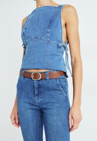 Denim top met een vierkante halslijn, zijkanten met strikken en lichtblauwe kleur. Gecombineerd met hoge blauwe jeans en een bruine riem met een gouden gesp.