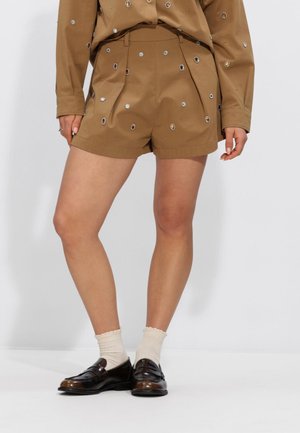 Femme portant un short marron et une chemise à manches longues assortie ornée de strass dispersés, accompagnée de chaussettes blanches et de mocassins marron foncé.