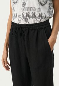 Pantalons en lin noir avec une taille élastique et un cordon de serrage. Comprend des poches latérales et une coupe décontractée, avec une texture lisse.