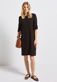 Robe marron, longueur genoux, avec des manches longues et des poignets roulés, assortie à des ballerines à imprimé léopard et un sac à main structuré beige.