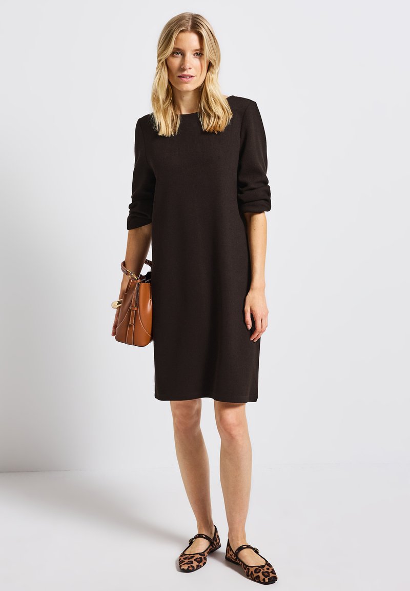 Robe marron, longueur genoux, avec des manches longues et des poignets roulés, assortie à des ballerines à imprimé léopard et un sac à main structuré beige.