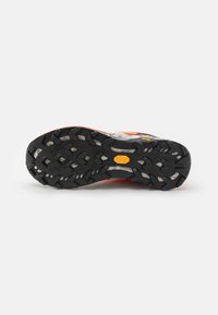 Semelle de chaussure de trail avec un motif de caoutchouc noir robuste, arborant un logo Vibram et des accents orange vif, conçue pour l'adhérence sur divers terrains.