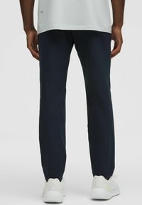 Pantalones deportivos azul marino hechos de tejido ligero, con un corte recto y un pequeño logo cerca del dobladillo, combinados con zapatillas blancas.