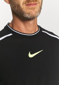 Musta urheilu paita pyöreällä kaula-aukolla, valkoiset raidat olkapäissä ja neonvihreä Nike-logo rinnassa.