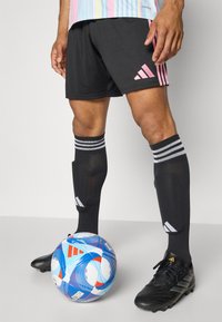 Czarne spodenki Adidas z różowym logo, czarne skarpetki do kolan w białe paski, czarne korki oraz piłka nożna w niebiesko-czerwono-białe wzory.