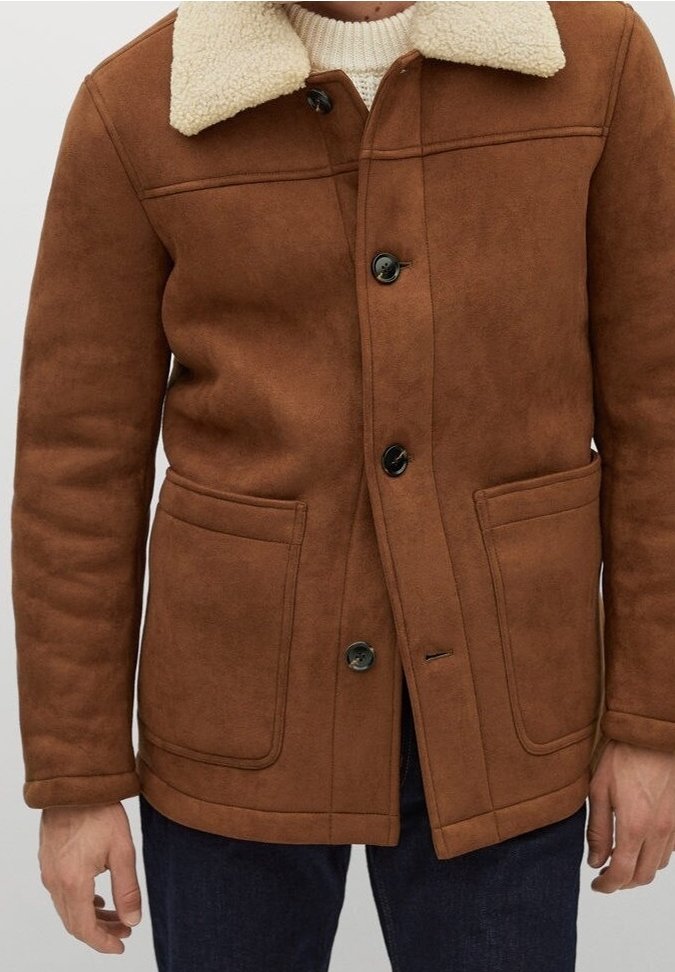 Brun, ruskindslignendejakke med en cremefarvet, faux-shearling krave; har sorte knapper, to forlommer og en lige kant.