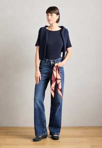 Jūras spēku īsām piedurknēm tops, īss cardigans, brīvi zili džinsi un drukāta šalle, ko piesien pie vidukļa. Gludas kurpes ar zemu papēdi.
