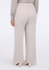 Vaaleanharmaat leveälahkeiset housut, joissa on teksturoitu kangas, korkea vyötärö ja lattiaan ulottuva pituus, yhdistettynä vaaleisiin korkokenkiin.