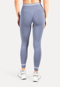 Sportleggings in meliertem Navy mit glatter Textur, hohem Bund und kontrastierenden Streifen am Knöchel, kombiniert mit weißen Turnschuhen.
