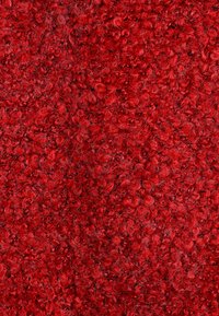 Roter Stoff mit einem strukturierten, geschlungenen Design, das lockige, weiche Fasern aufweist. Die Oberfläche ist dicht und schafft ein reiches, lebendiges Erscheinungsbild.