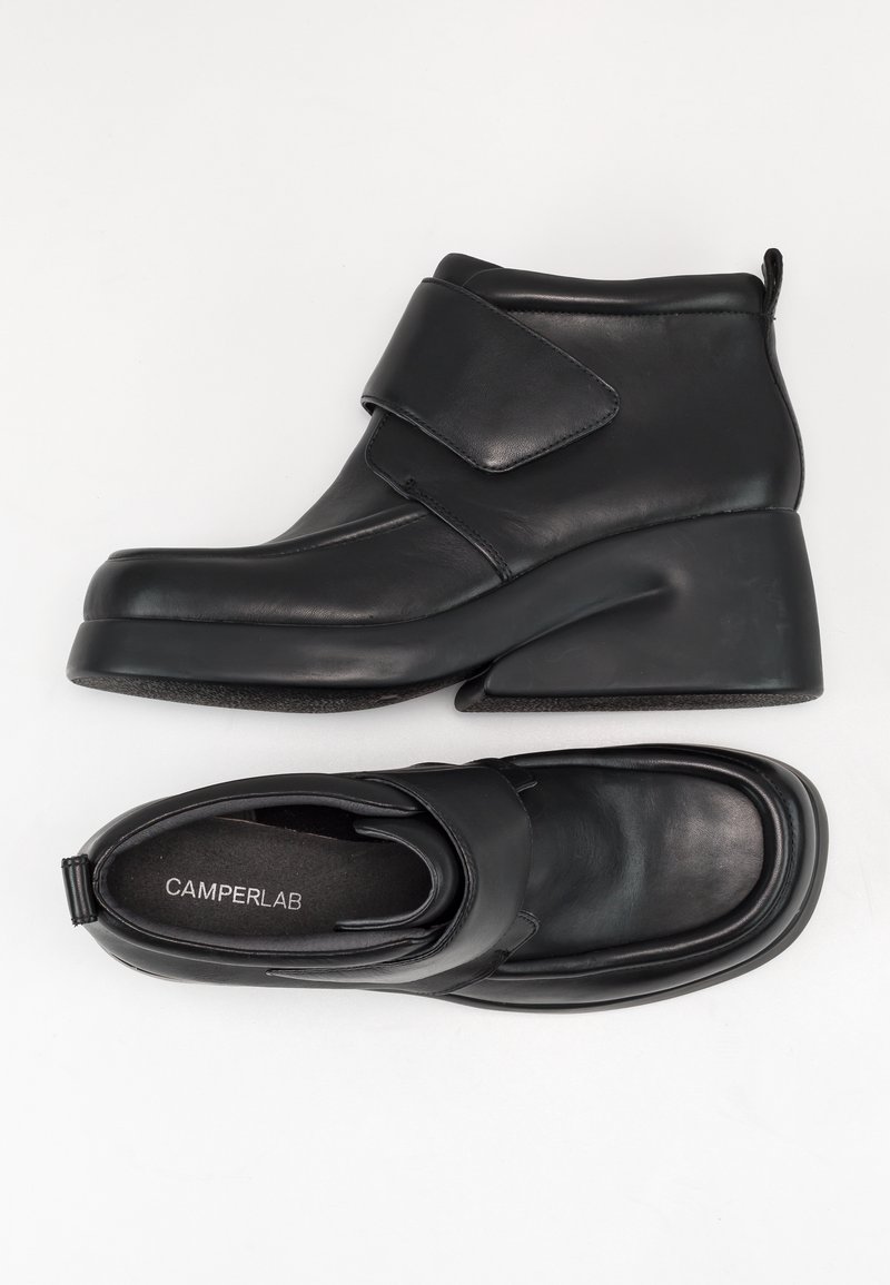 Bottines en cuir noir avec talons compensés et larges bandes velcro, une botte vue de côté, l’autre vue de dessus avec semelle intérieure « CAMPERLAB ».