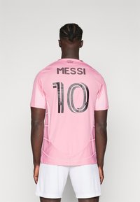 Lyserød fodboldtrøje med navnet "MESSI" og nummeret "10" i sort skrift. Kortærmet og lavet af letvægtsmateriale, der er velegnet til sport.
