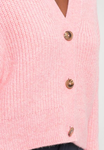 Rosa gestrickte Jacke mit V-Ausschnitt, ausgestattet mit drei runden, beigen Knöpfen entlang der Vorderseite und einem gerippten Saum. Weiche Textur und verkürztes Design.