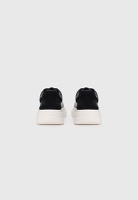 Black sneakers with a smooth leather upper and cushioned white soles. Rounded shape with no visible laces, featuring a padded collar.