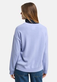 Helles lila Sweatshirt aus weichem Strickmaterial mit Rundhalsausschnitt, überschnittenen Schultern und gerippten Bündchen. Seitliche Schlitze am Saum sorgen für zusätzliche Details.