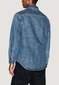 Camicia in denim di blu medio, con colletto, maniche lunghe e polsini con bottoni. Orlo curvo con dettagli di cucitura a vista.