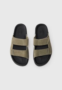 Olivenfargede semskede sandaler med to brede stropper, kontrasterende sokkermørk gummisåle og teksturerte overflateakenter. Minimalistisk design.