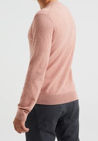 Mäns långärmad tröja i mjuk rosa stickad kvalitet med rund halslinning och ribbad nederkant, kombinerad med mörkgrå byxor.