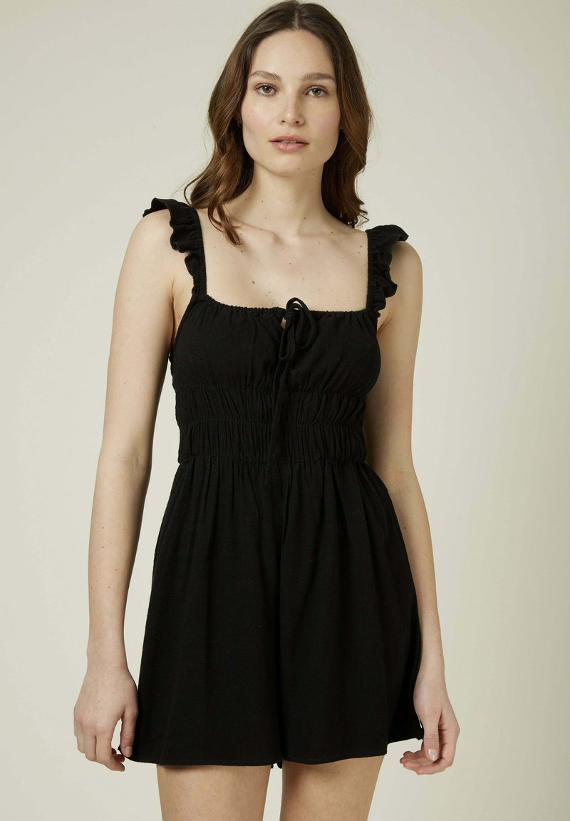 Rompers noirs avec des bretelles froncées, un corsage smocké et un détail de nœud ajustable à l'avant. Tissu doux et léger.