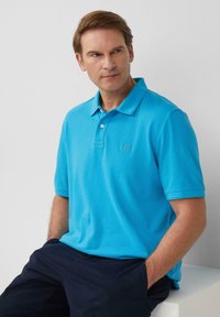 Polo bleu clair avec un col, des manches courtes et un petit logo sur la poitrine. Porté avec un pantalon bleu marine. Texture lisse.