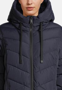 Dunkelblaue Steppjacke mit einem gesteppten Design, hohem Kragen, verstellbaren Zugbändern und einem Frontreißverschluss.