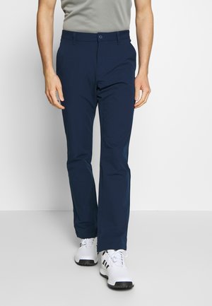 Granatowe chinosy z elastycznego materiału z zapięciem na guzik, kieszeniami bocznymi i prostymi nogawkami, w połączeniu z białymi sneakersami. Gładka tekstura.