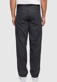 Pantalones de mezclilla negros con un ajuste holgado y dobladillos acampanados. Presenta dos bolsillos traseros y detalles de costura sutiles. Llevados con zapatillas blancas.
