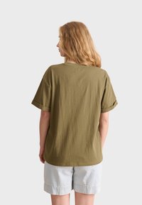 T-shirt verde oliva a maniche corte con vestibilità rilassata e orli arrotolati, realizzata in morbido tessuto di cotone. Design casual con scollo rotondo.