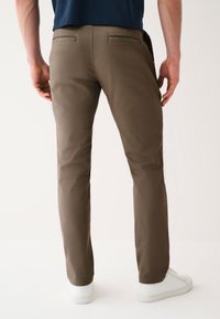 Brown trousers with a slim fit, featuring two back pockets and a smooth texture, paired with white sneakers against a neutral background.