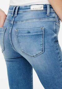 Jeans ajustados de mezclilla azul claro, con una cintura de altura media, dos bolsillos traseros, un diseño cosido y una sutil textura deslavada.