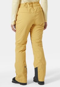 Geel skibroek met een textuurafwerking, voorzien van een cinch-taileband, zijzakken en zwarte accenten op de onderbenen. Duurzaam materiaal ontworpen voor wintersport.