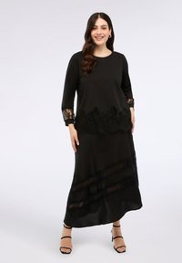Abito nero con dettagli in pizzo sull'orlo e sulle maniche, maniche lunghe, scollatura rotonda e una gonna fluida con design a strati.