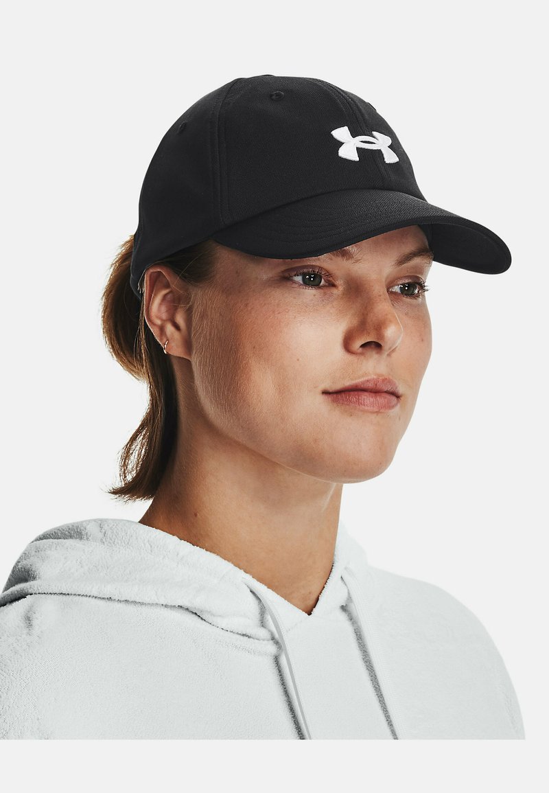 Melnā beisbola cepure no auduma ar izliektu vizuļu, priekšā ir izteiksmīgs balts Under Armour logotips. Mīksta tekstūra.