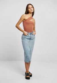 Brun en skulder topp, tettsittende, kombinert med høyt liv lys blå denim midi skjørt, med rett silhuett og lommedetaljer. Svart plattform sandaler.
