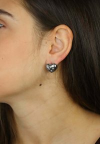 Kolczyki w kształcie serca w kolorze czarnym z metalicznymi akcentami, na tle jasnej karnacji; jeden kolczyk ma wzór gwiazdy.