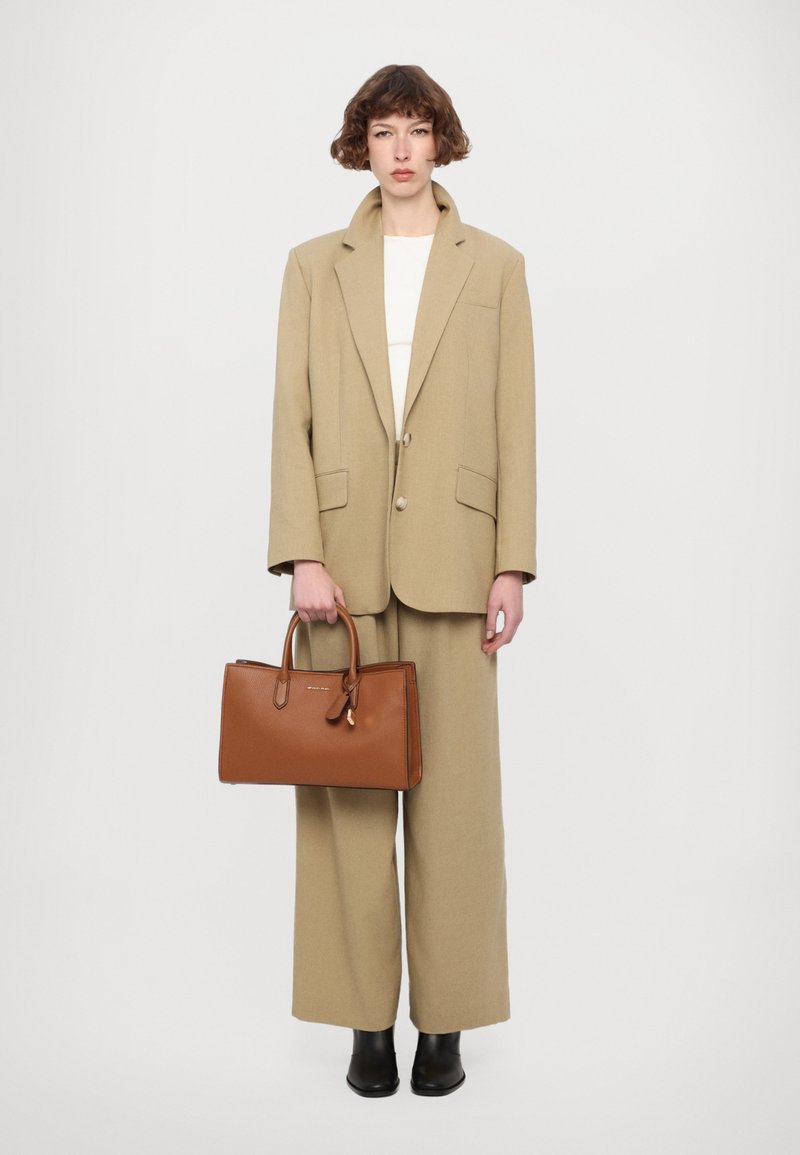 Blazer oversize beige e pantaloni a gamba larga coordinati, insieme a una borsa in pelle marrone texture. Stivali neri alla caviglia completano l'outfit.