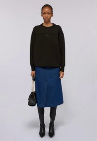 Svart sweatshirt med rund halsringning, kombinerad med en blå denimkjol i midilängd med framfickor. Svarta knähöga stövlar och en svart handväska.