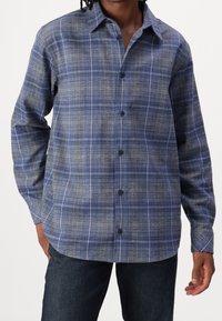 Camicia a quadri blu realizzata in tessuto tessuto, con maniche lunghe, colletto a punta e chiusura con bottoni. Motivo testurizzato con dettagli bianchi.