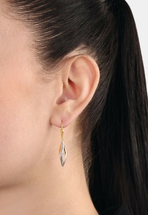 Pendientes en forma de hoja de oro y plata con un acabado pulido, colgando de un pequeño gancho de oro, mostrados contra la oreja de un modelo con cabello oscuro.