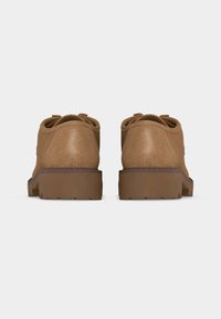 Paire de chaussures en suède beige avec semelles épaisses en caoutchouc marron, vues de dos sur un fond gris clair uni.