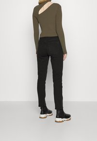 Bodysuit de manga larga en verde oliva con textura de canalé y corte lateral, combinado con pantalones ajustados negros y botas negras de tobillo con suelas blancas.