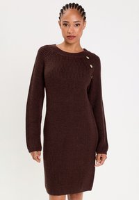 Brown ribbed knit dress with a round neckline, long sleeves, and a side button detail. Smooth texture with a fitted silhouette.