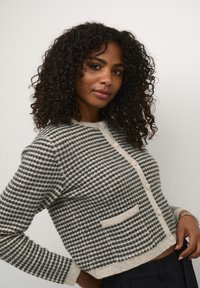 Knit cardigan in cream and dark green stripes, featuring a button closure, round neckline, and a small front pocket. Soft texture.